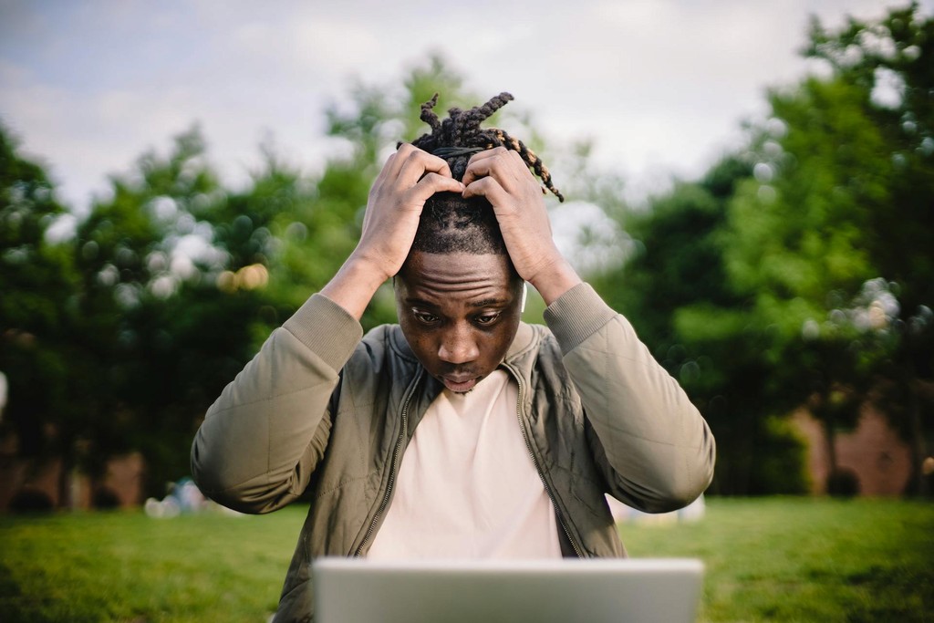 a concerned man holding his head in hands, looking into his laptop