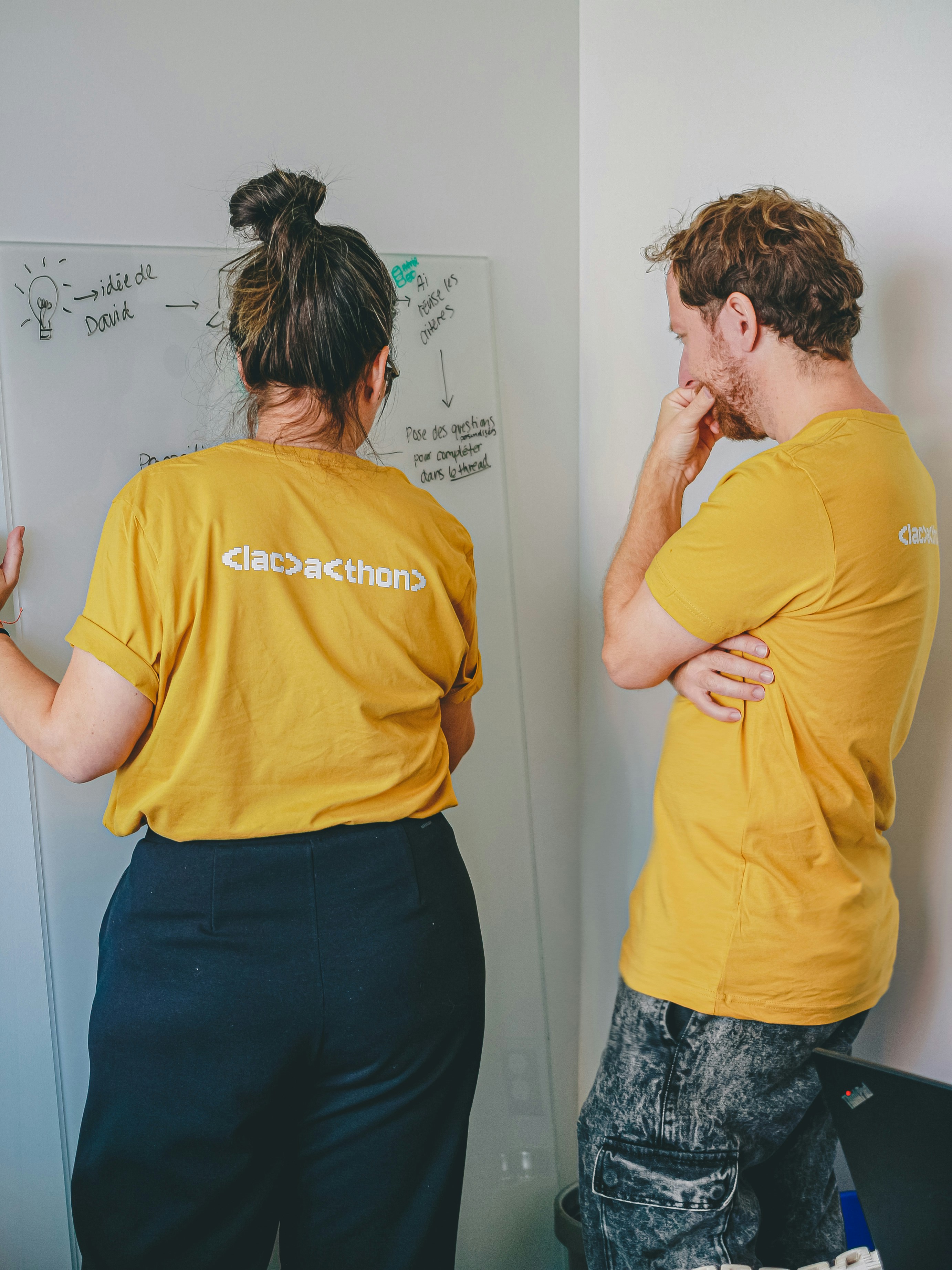 Two people in yellow shirts looking at whiteboard.