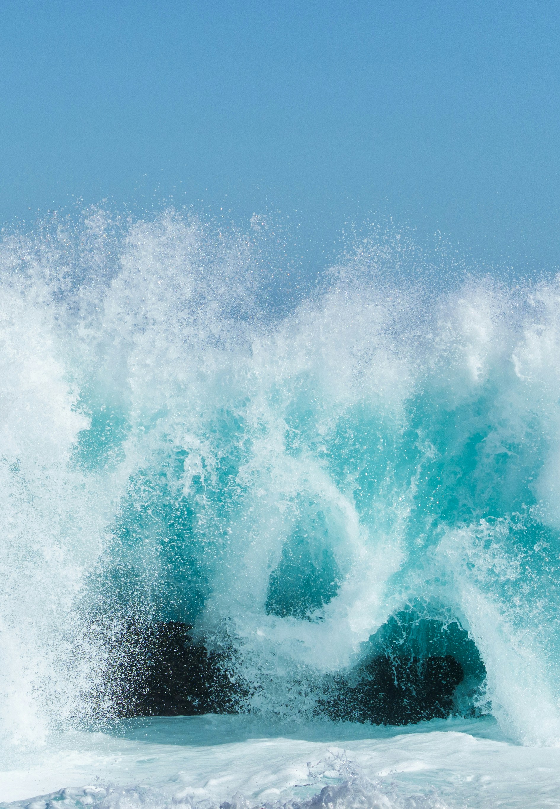 Turquoise ocean wave crashing against dark rocks
