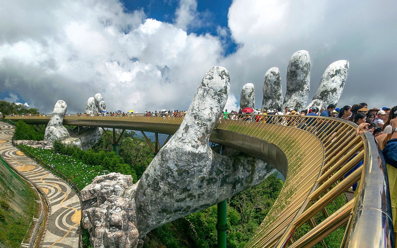 People walking on the Golden Bridge held by giant hands in Ba Na Hills, Vietnam.