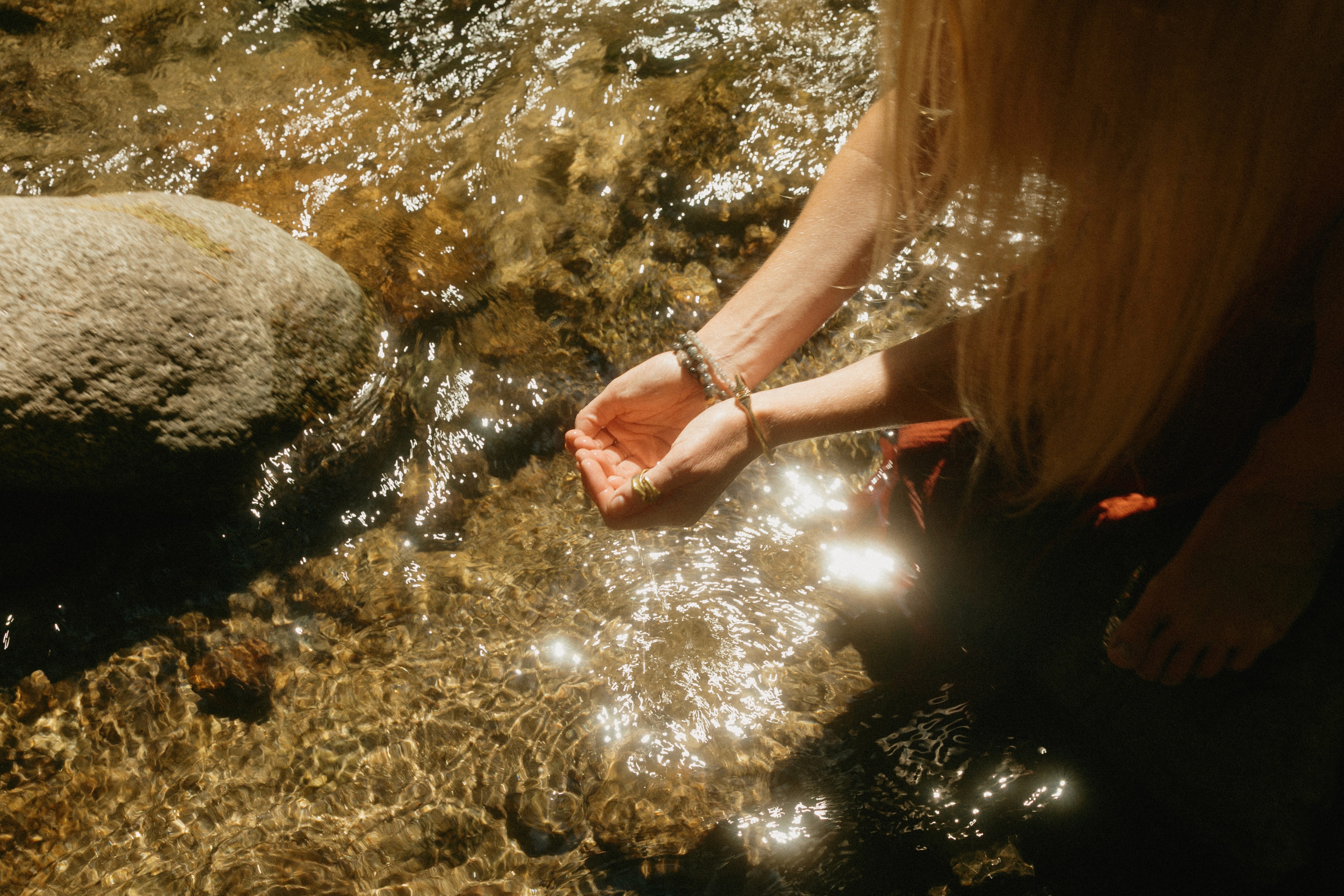 Hands cupped in sparkling stream water representing cleansing and somatic grounding during the summer solstice retreat