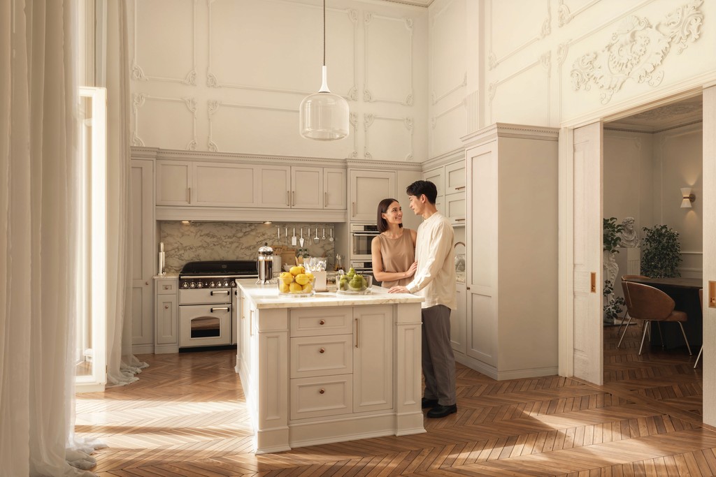 Luxury Parisian kitchen interior design with shaker-style cabinetry in warm greige, marble worktop kitchen island, marble slab backsplash, range cooker, herringbone parquet flooring, and double-height ornate plaster moulded walls