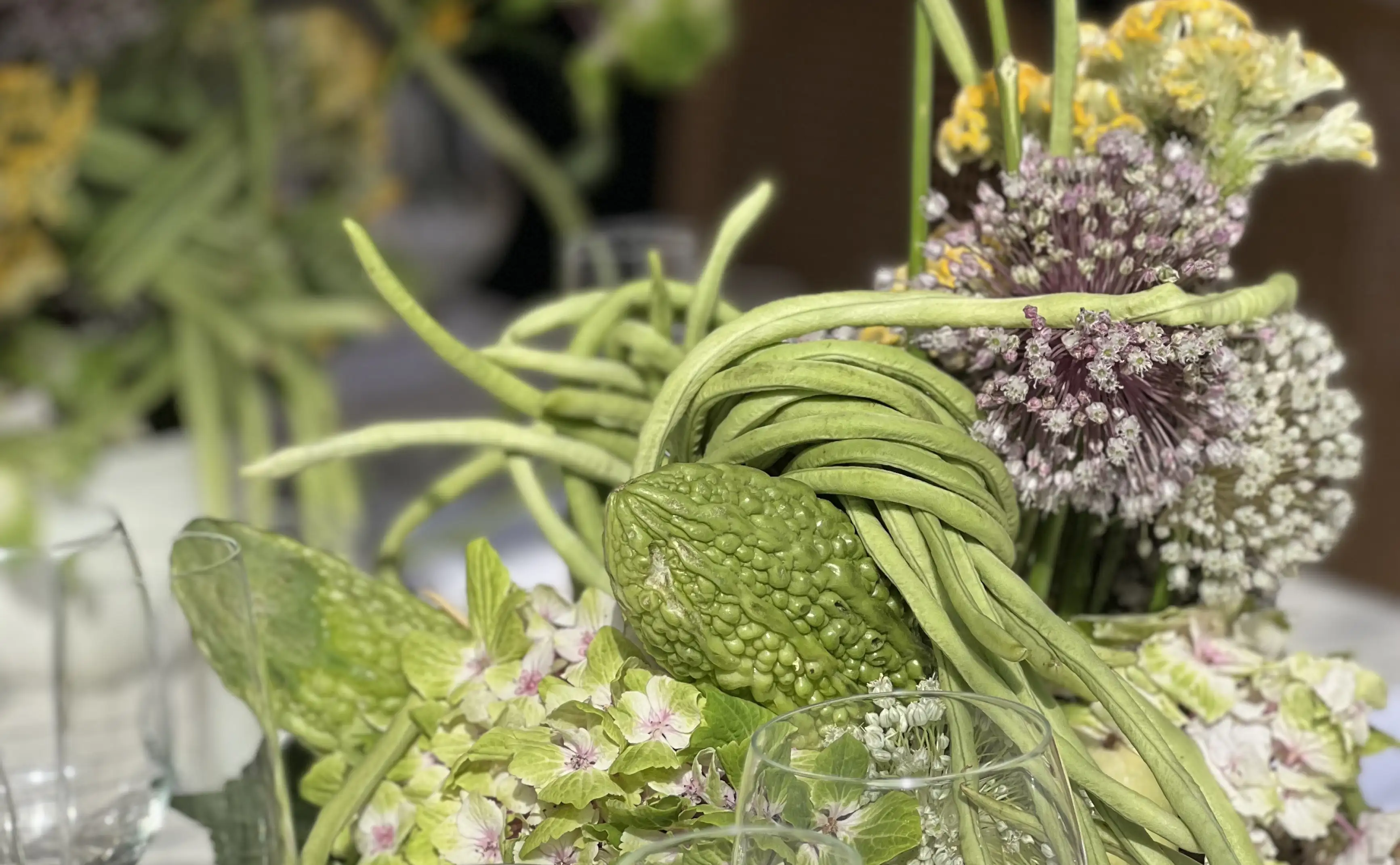 Detalle de composición botánica con flores esféricas, follaje verde y texturas naturales en primer plano.