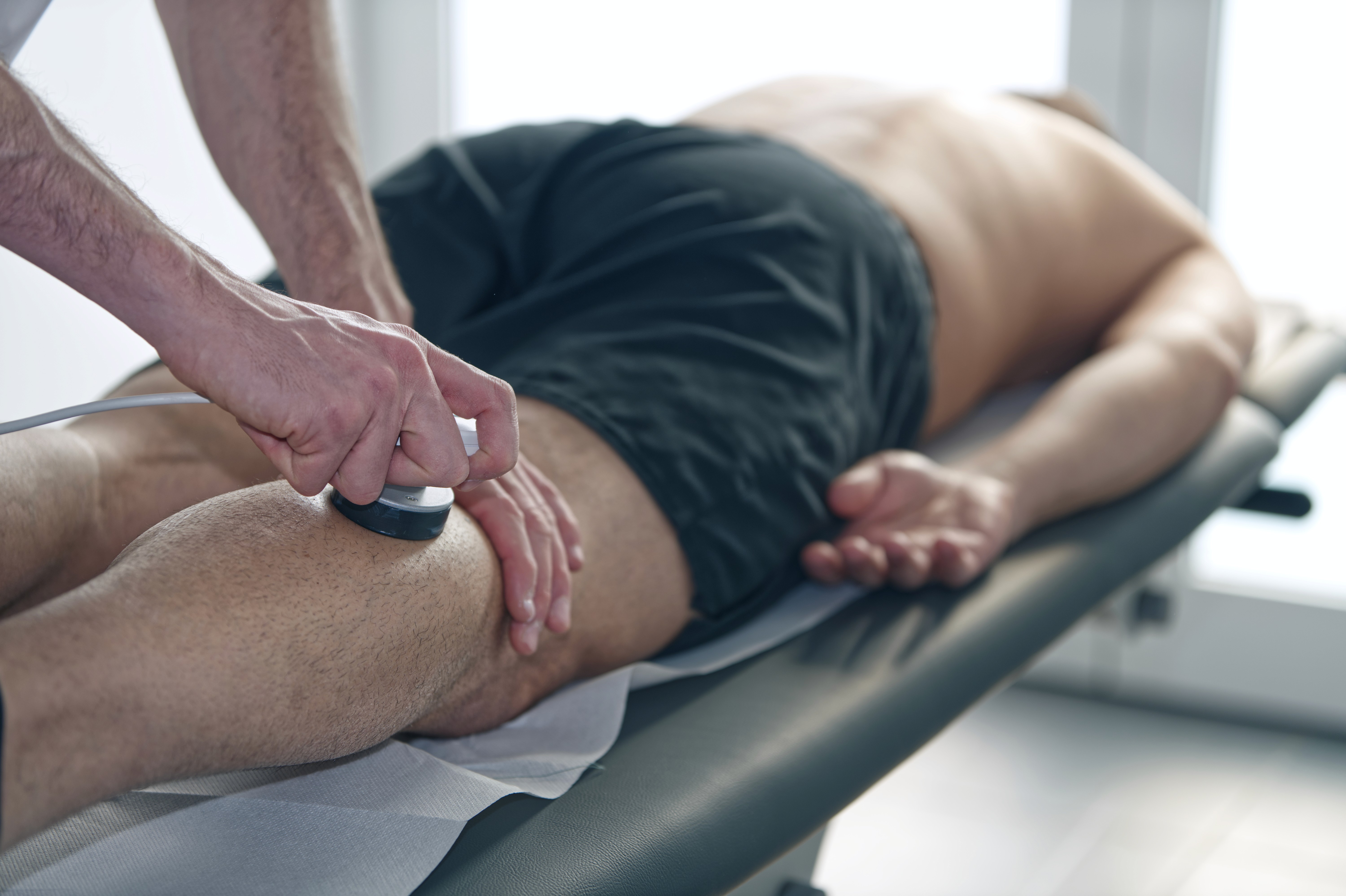 A man and woman sit on beige chairs in a modern room with a red paneled wall. A red pendant light hangs above a wooden coffee table between them.