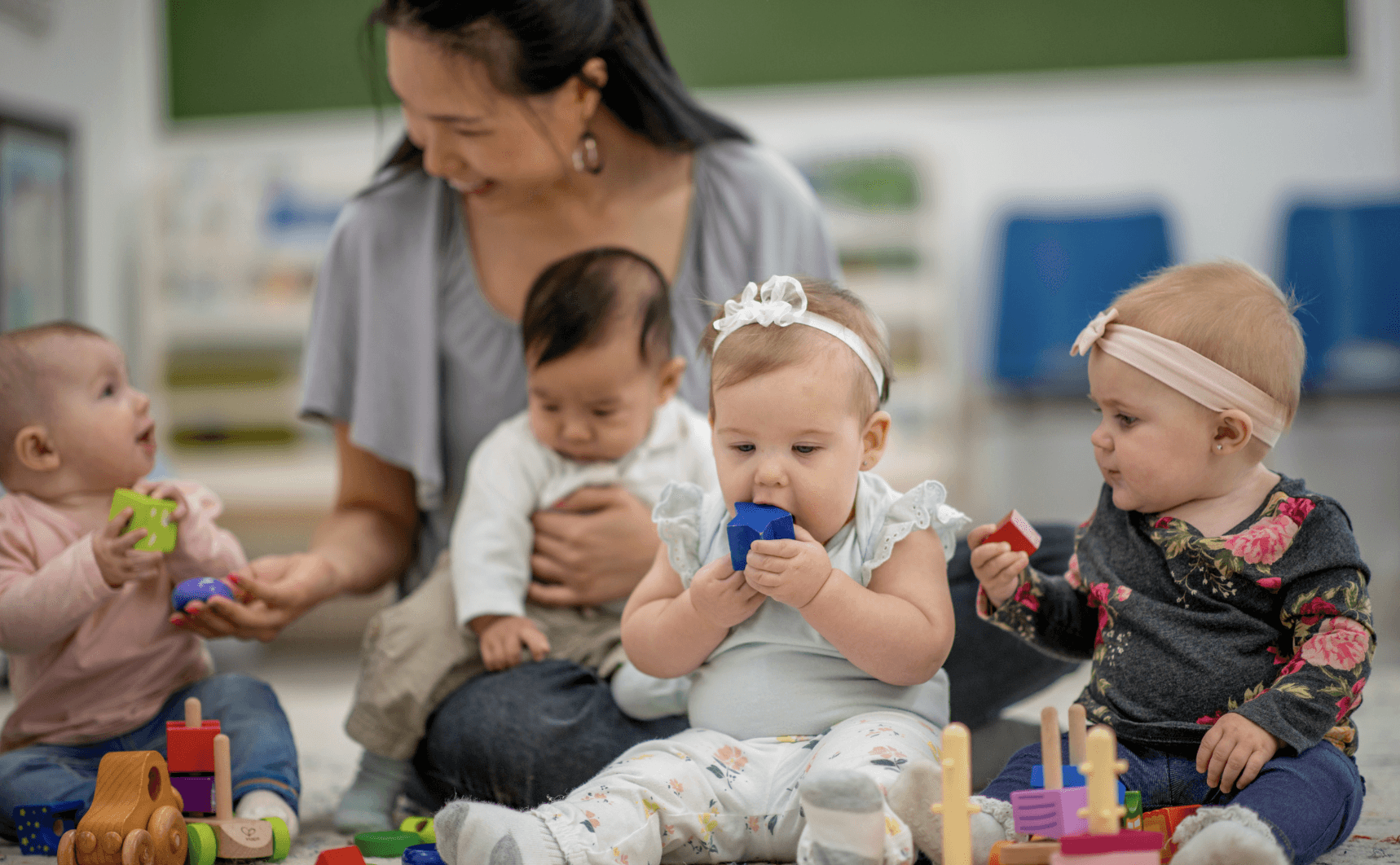 A teacher interacting with 4 infants on the play area at a child care center