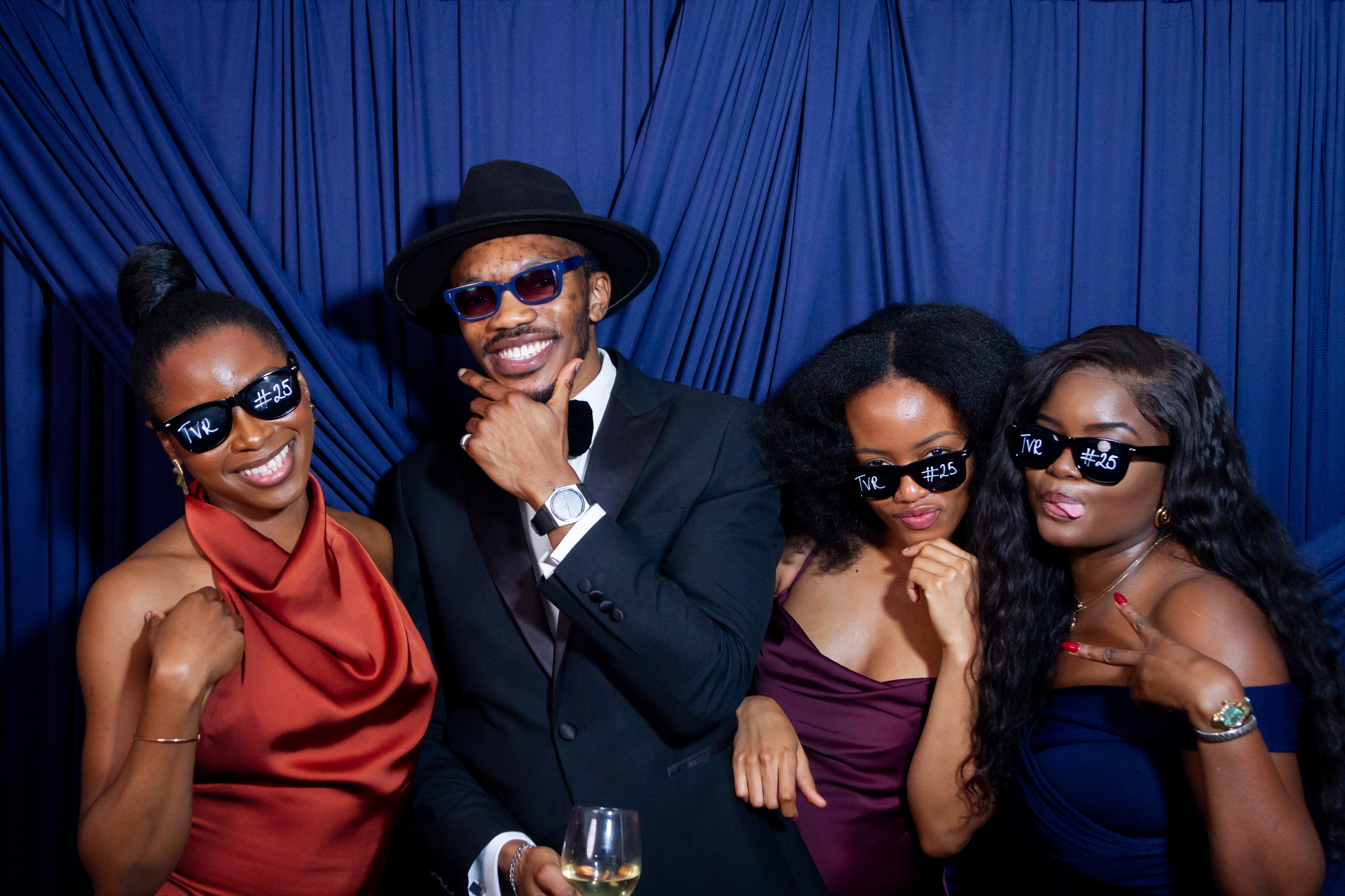 Four stylish friends in formal wear and sunglasses pose for a photo.