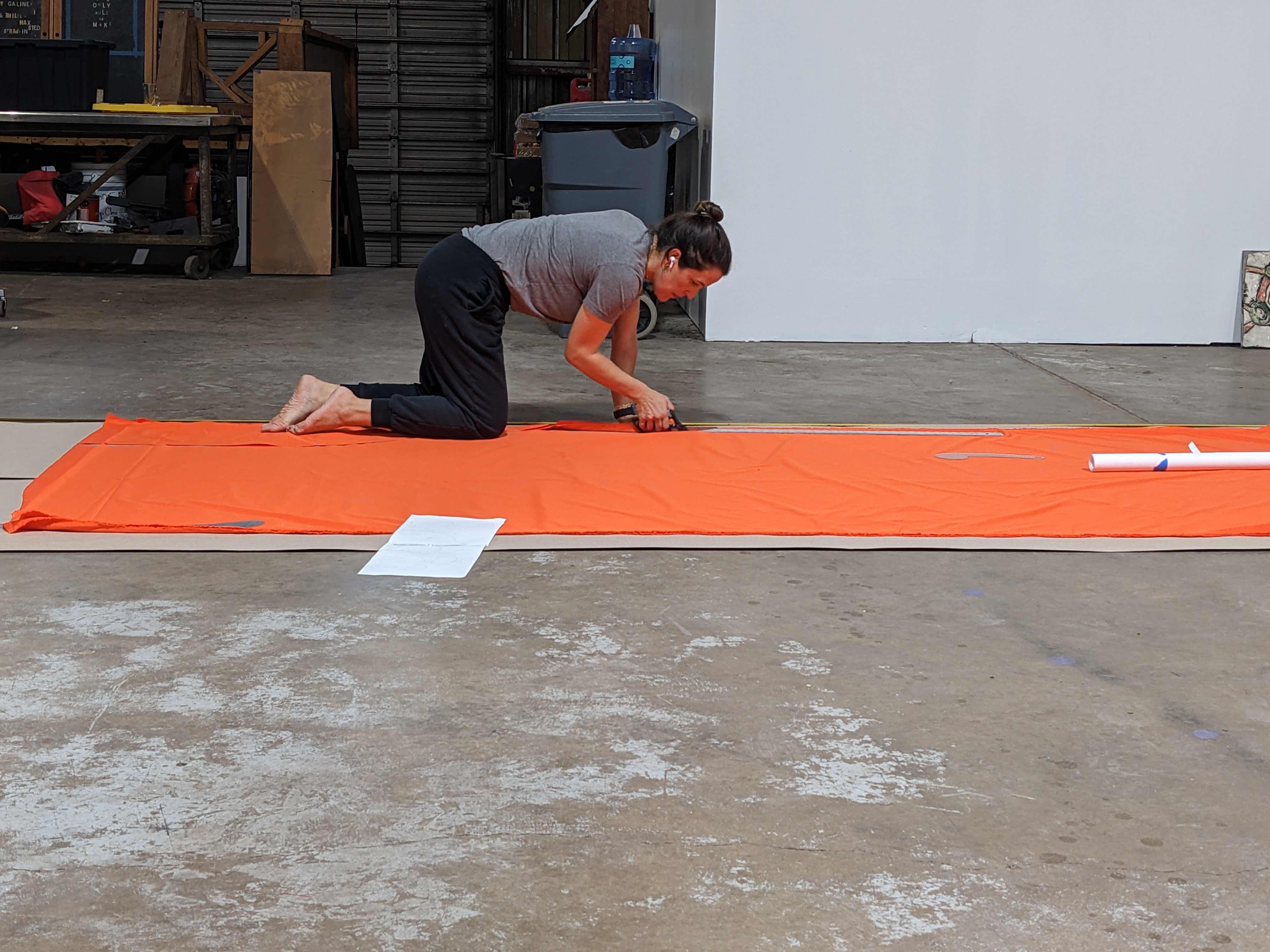 A person kneeling on a bright orange mat, working on a project in a garage space.