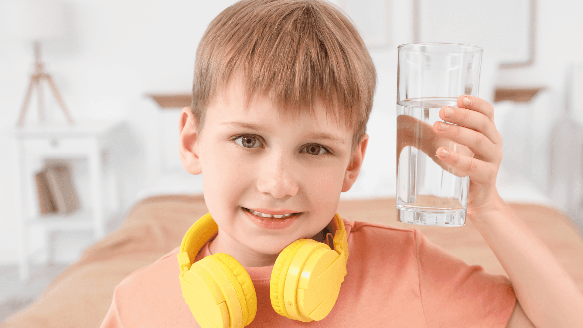 A young boy smiling, holding a glass of water with headphones around his neck, looking happy after listening to HushAway®’s Sound Sanctuary.