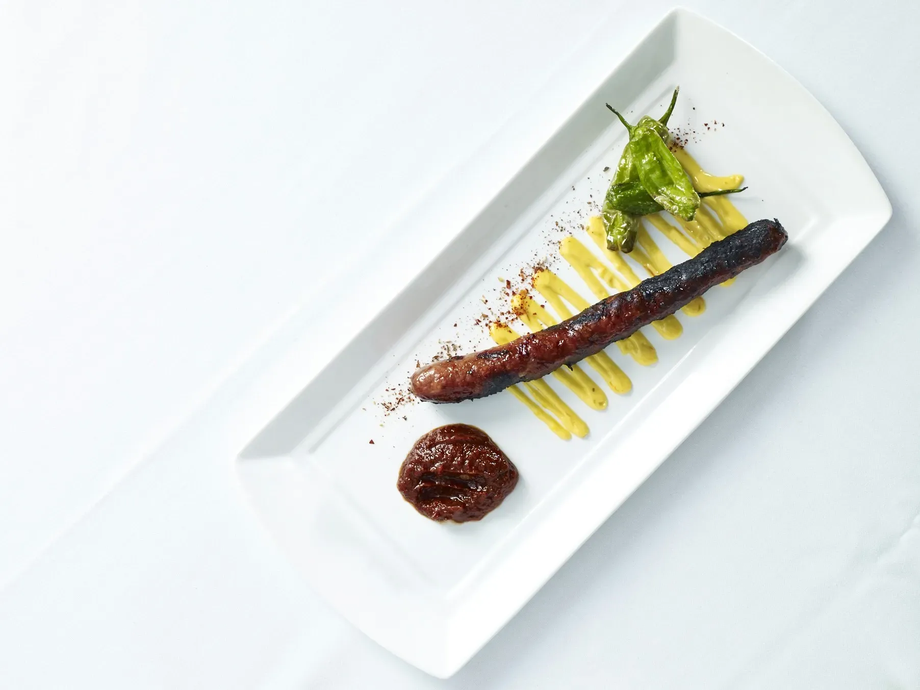 Grilled octopus plated with asparagus and sauce on a modern white dish.