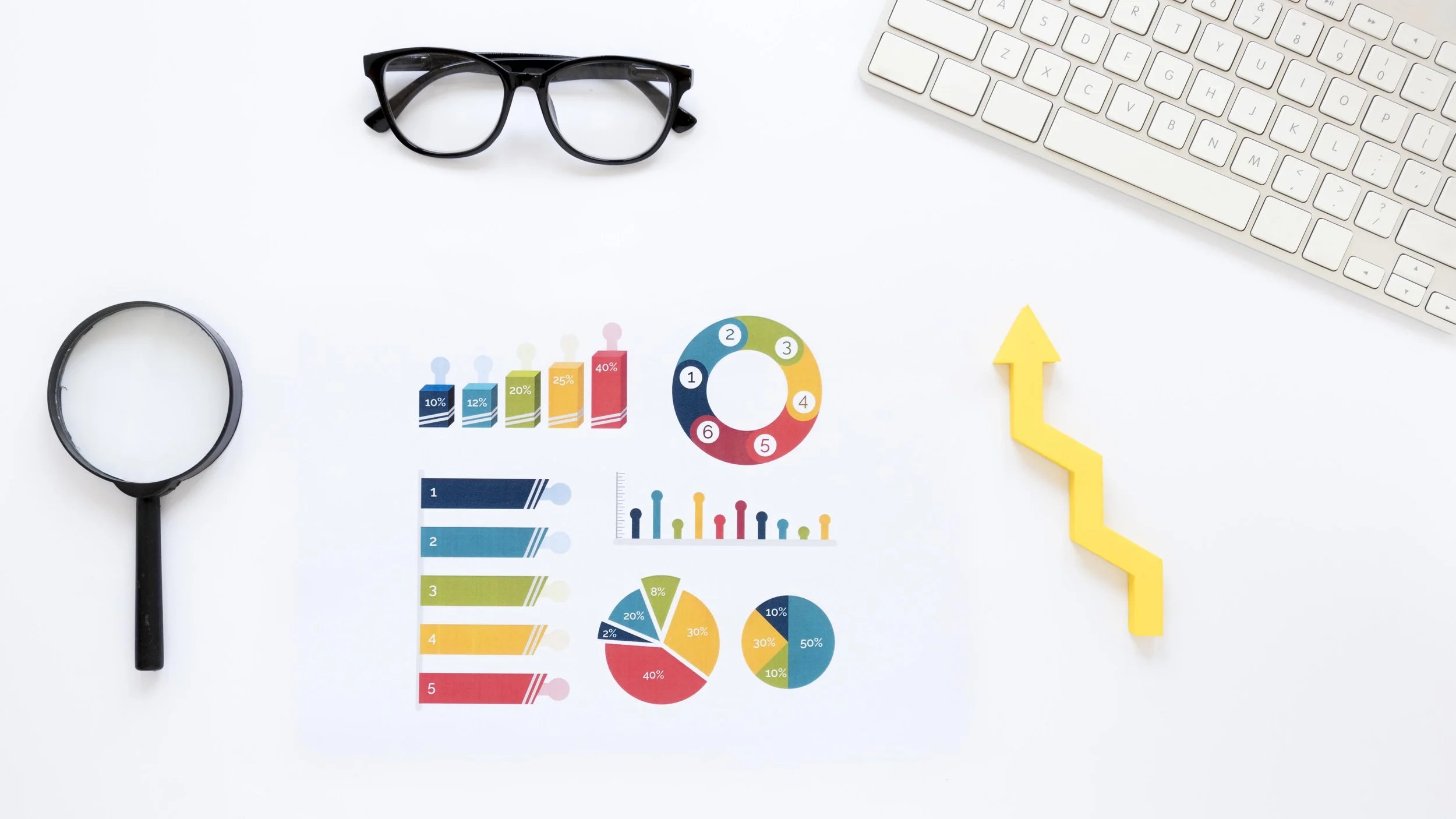 Paper graph with magnifier and glasses next to a keyboard