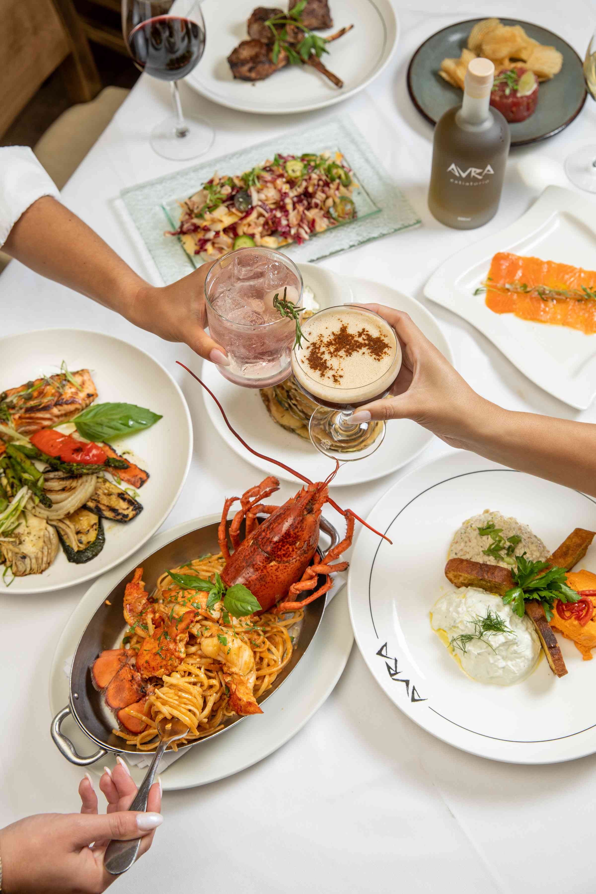 A table is set with various dishes, including seafood and sides, as hands reach for the food.