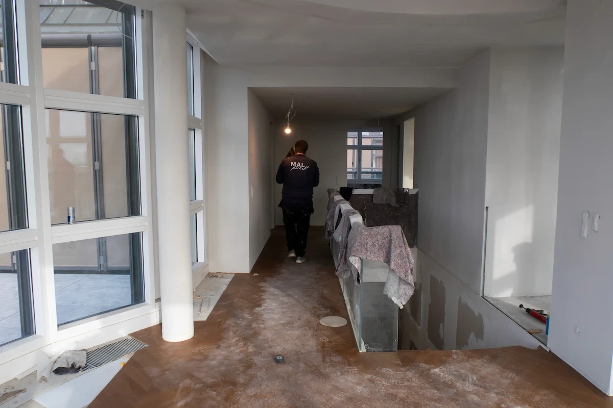 Parkettboden-Sanierung in modernem Wohnraum – Handwerker von MAL Parkett arbeitet in einem lichtdurchfluteten Flur während der Renovierung.