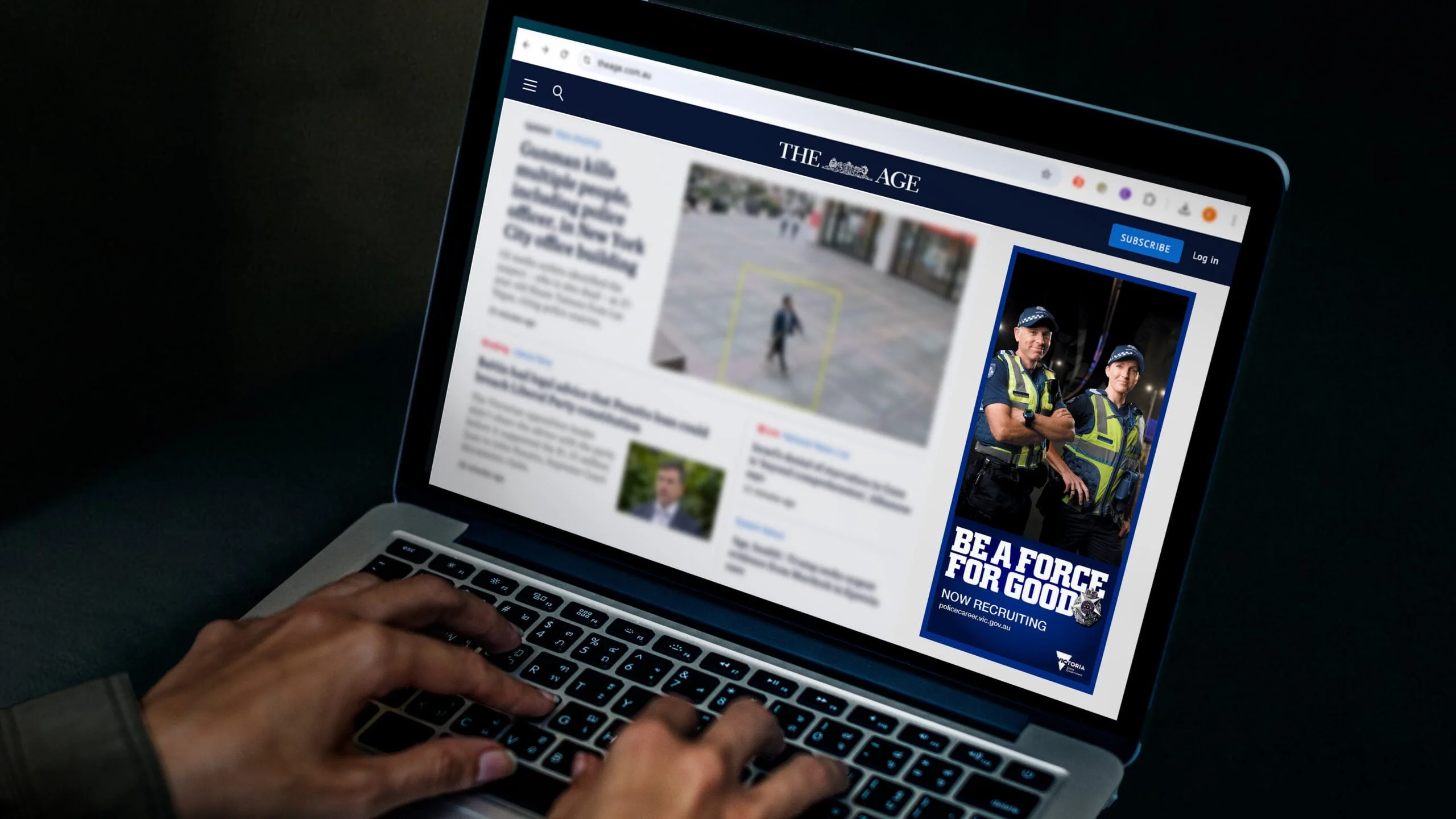 Laptop showing The Age website with a Victoria Police 'Be a force for good. Now recruiting' banner ad beside the news