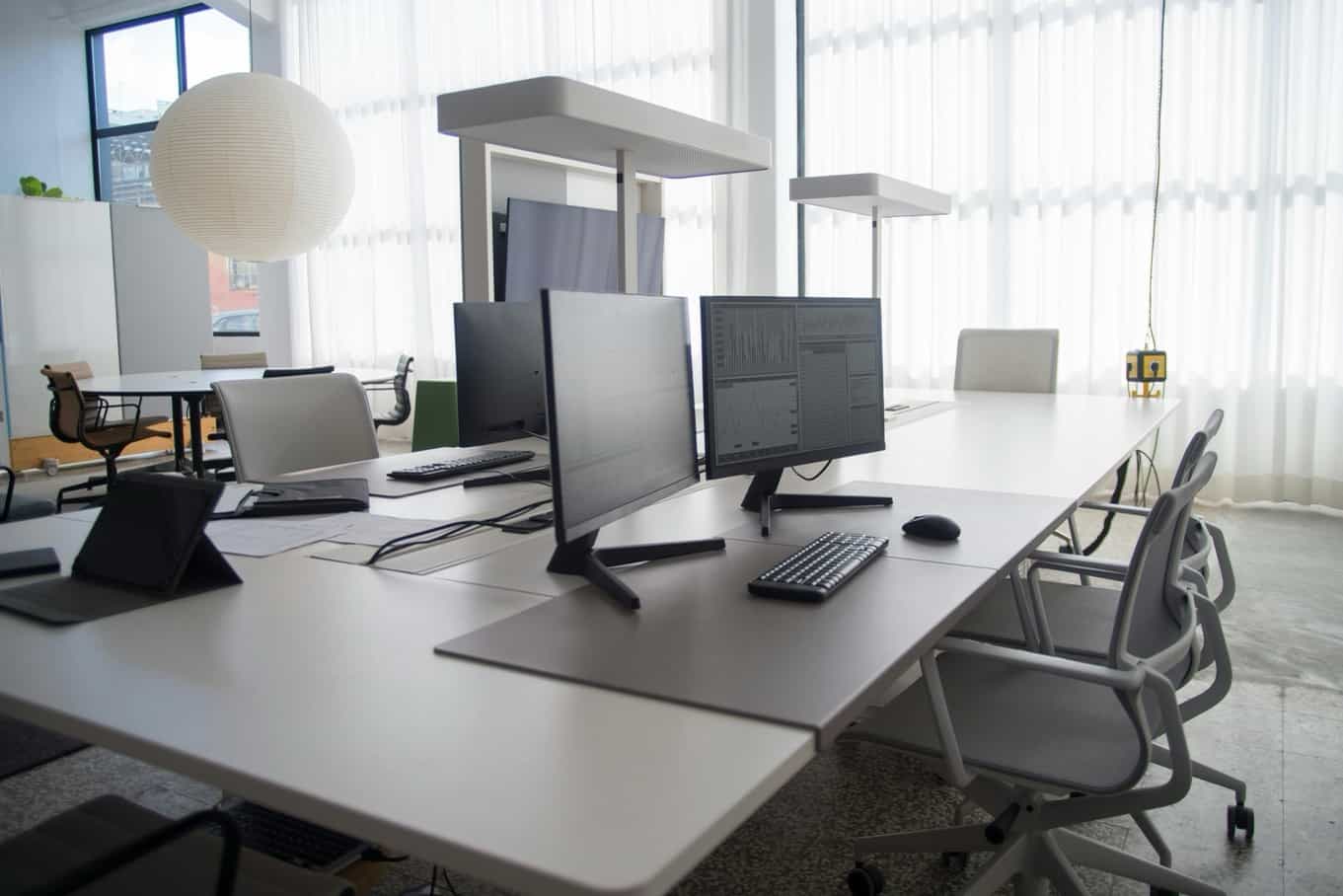 Modern, empty office desk setup. A large computer monitor displays complex financial charts and data dashboards. A mesh office chair is visible in the foreground, with the New York City Office address listed below.