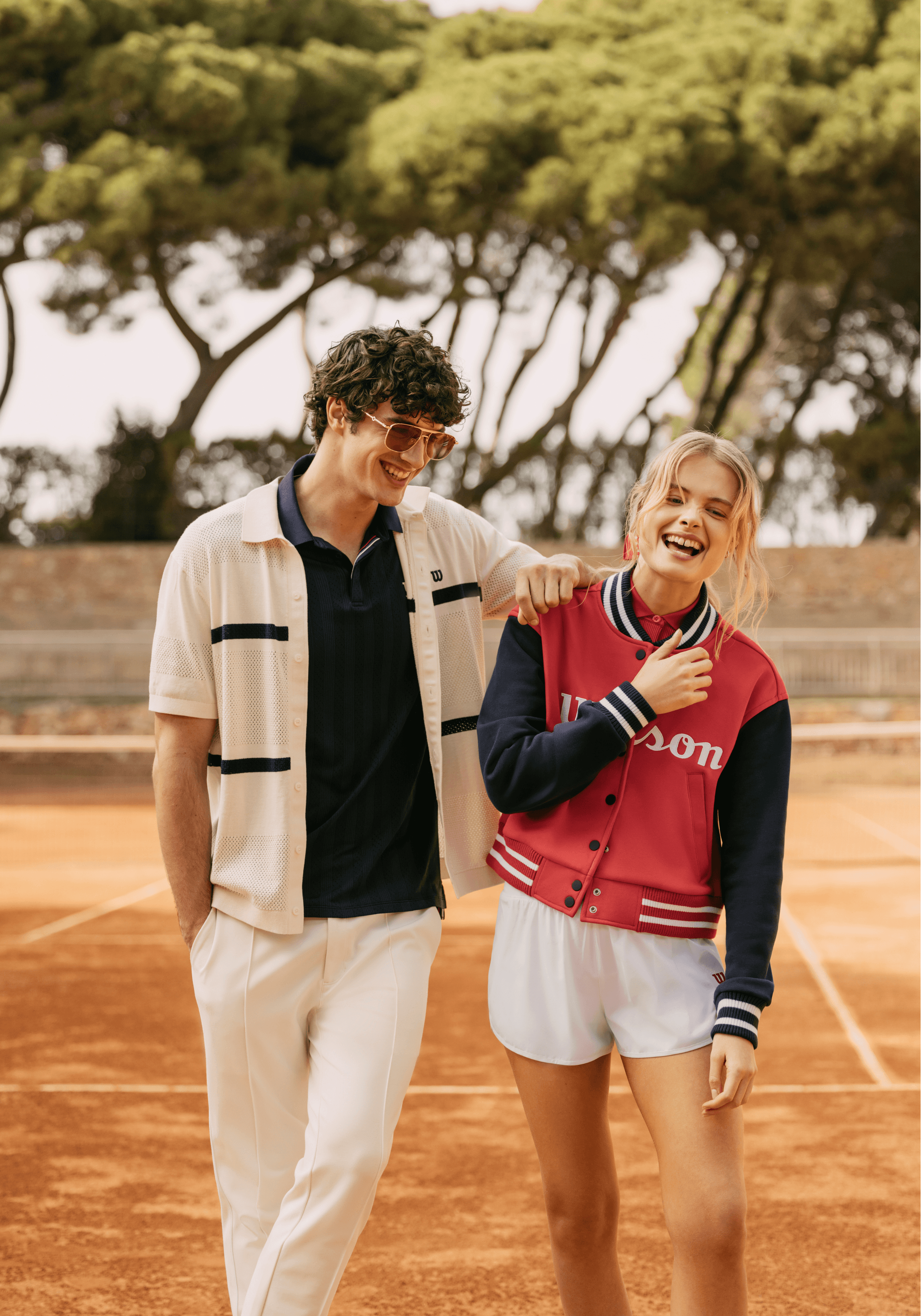 Deux mannequins habillés en Wilson Sportstyle sur un court de tennis, portant polo, short de tennis et blouson