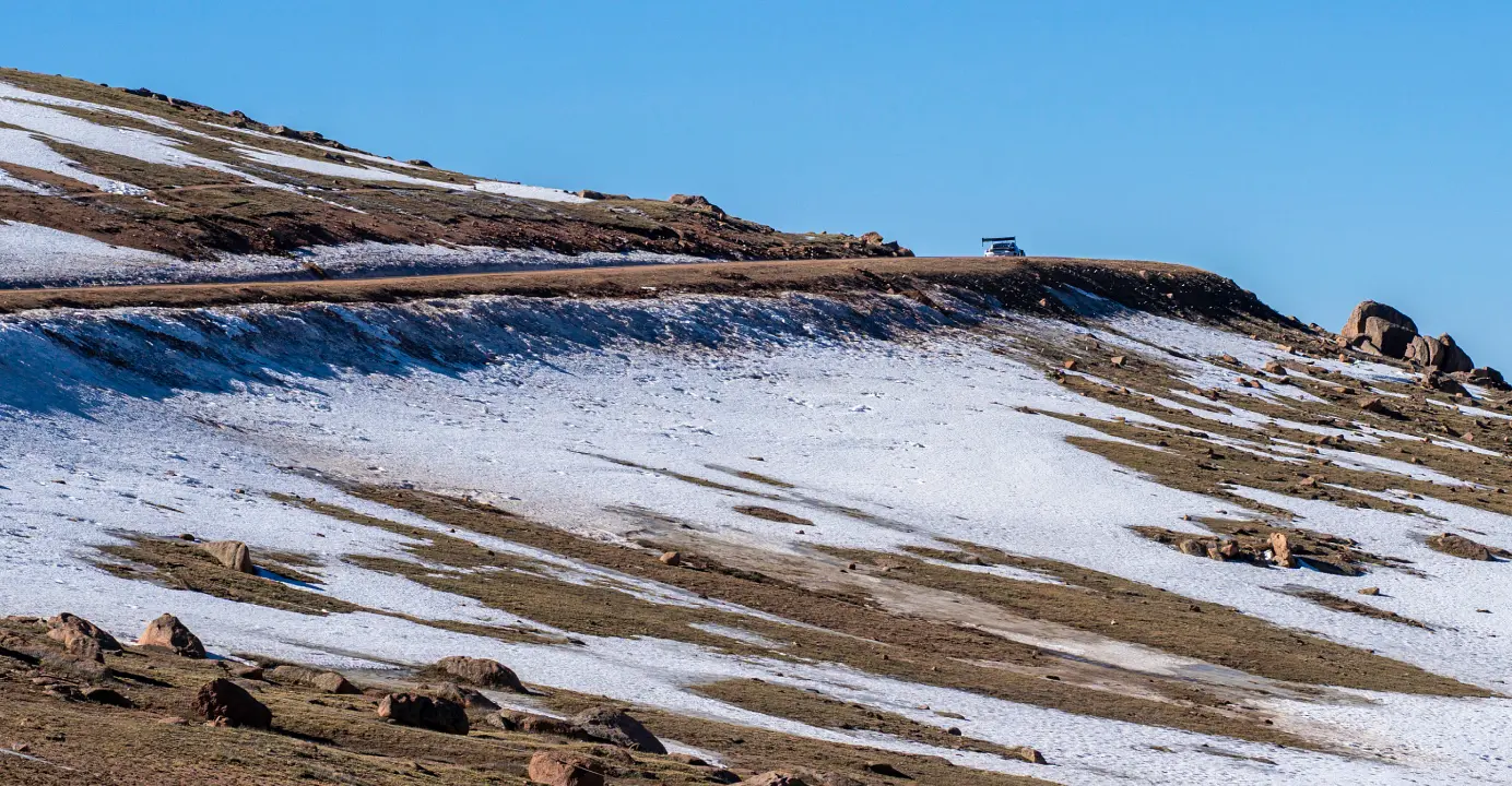 A race car driving up Pike Peaks mountain, with snow on the ground.