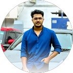 Portrait of a young woman with dark hair and green eyes, wearing a black top and gold necklace, set against a neutral background.