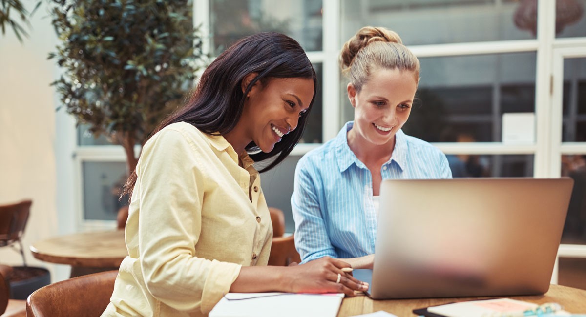 Two colleagues smiling while working together on a laptop at a bright office table