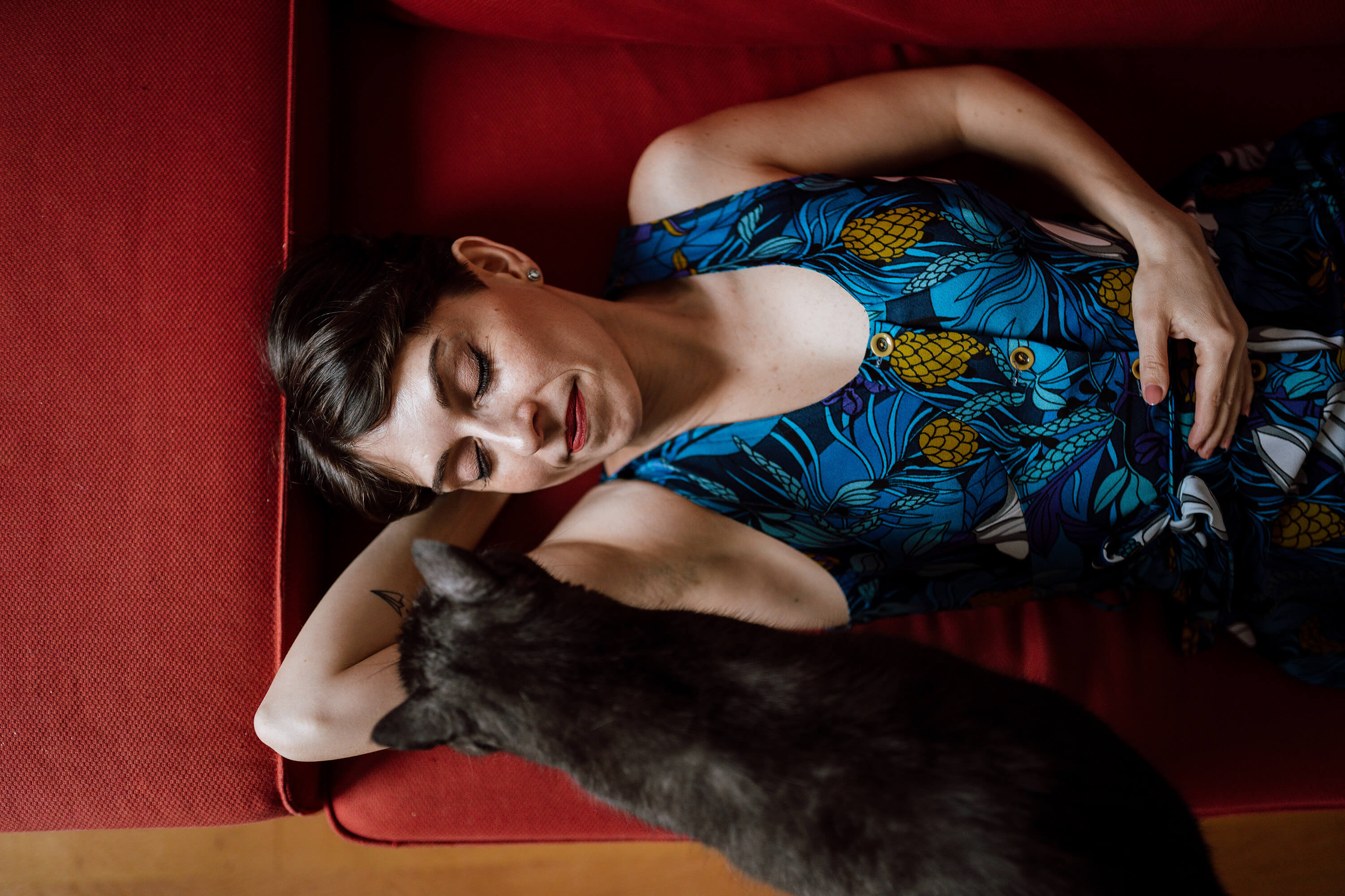 Francesca Introvaia relaxing on a red couch with a grey cat.