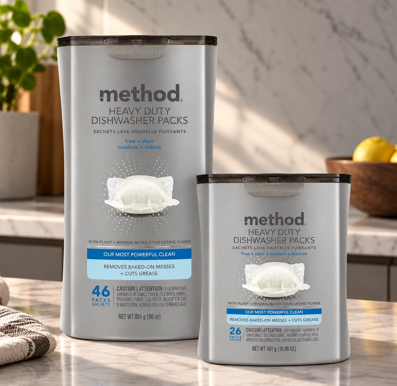 Tall and short silver dishwasher pack canisters side by side on a marble counter, a bowl of lemons behind