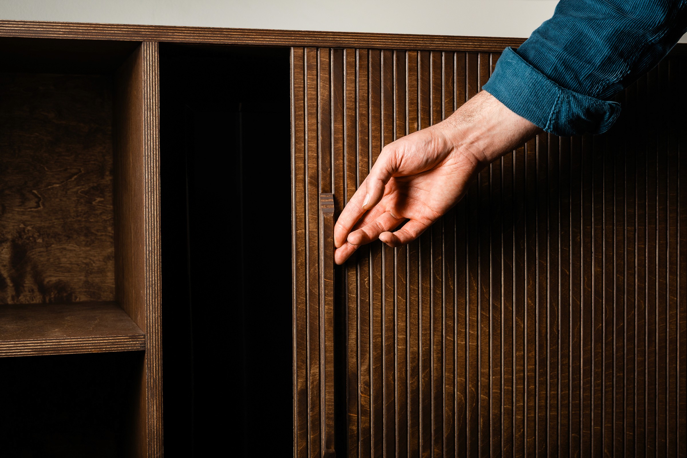een hand sluit een roldeur van een handgemaakt tv-meubel waarbij de tv weggewerkt wordt achter de roldeur
