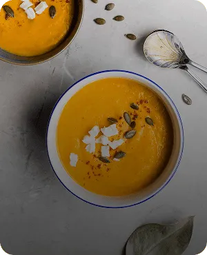 Creamy pumpkin soup served in a bowl, topped with seeds and a drizzle of cream.