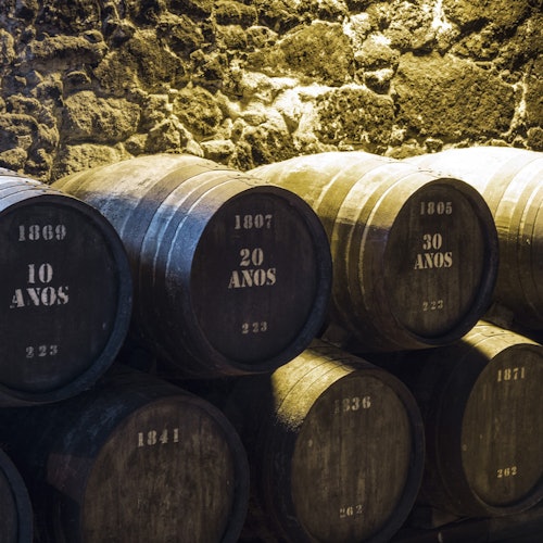 Wooden barrels labeled with ages in years (10, 20, 30) stacked against a stone wall under warm lighting.