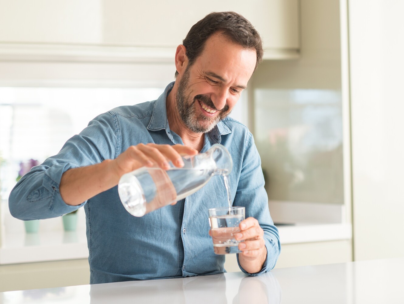 man pouring a glass of water to make sure that he is hydrated enough while taking prescribed medication for weight loss