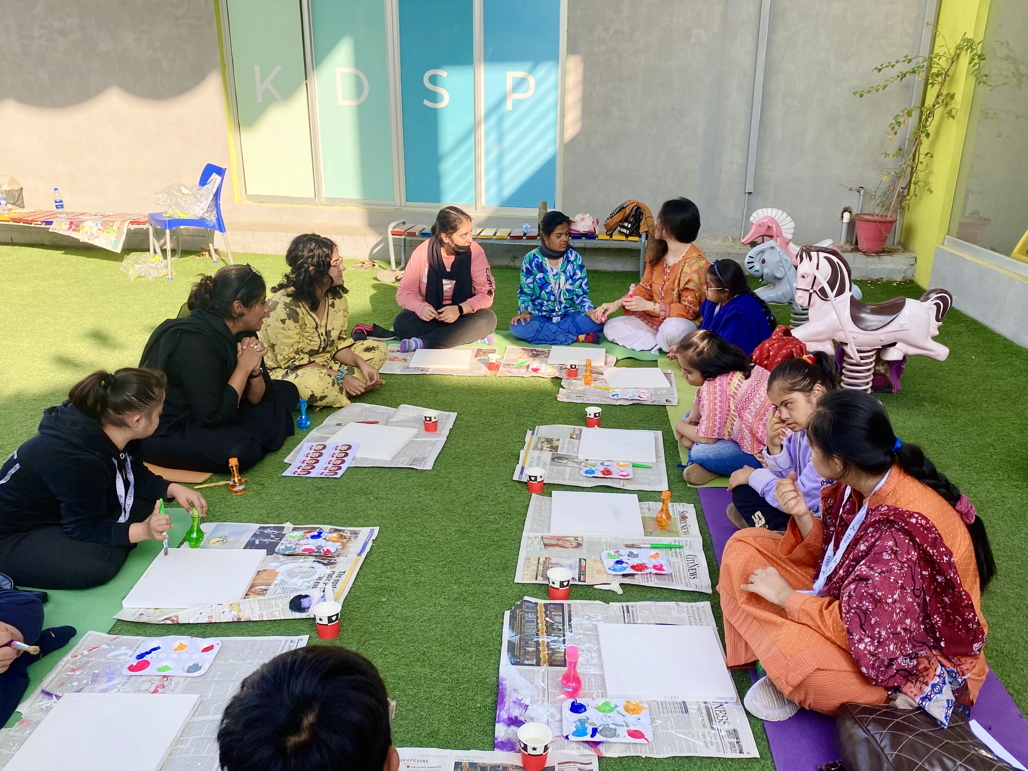 A group of children with down syndrome creating artwork sitting around art supplies, this time within an outdoor setting