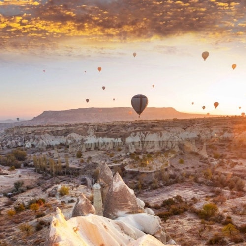 热气球在日落时分漂浮在岩石地貌上空,天空中飘着一些云朵。