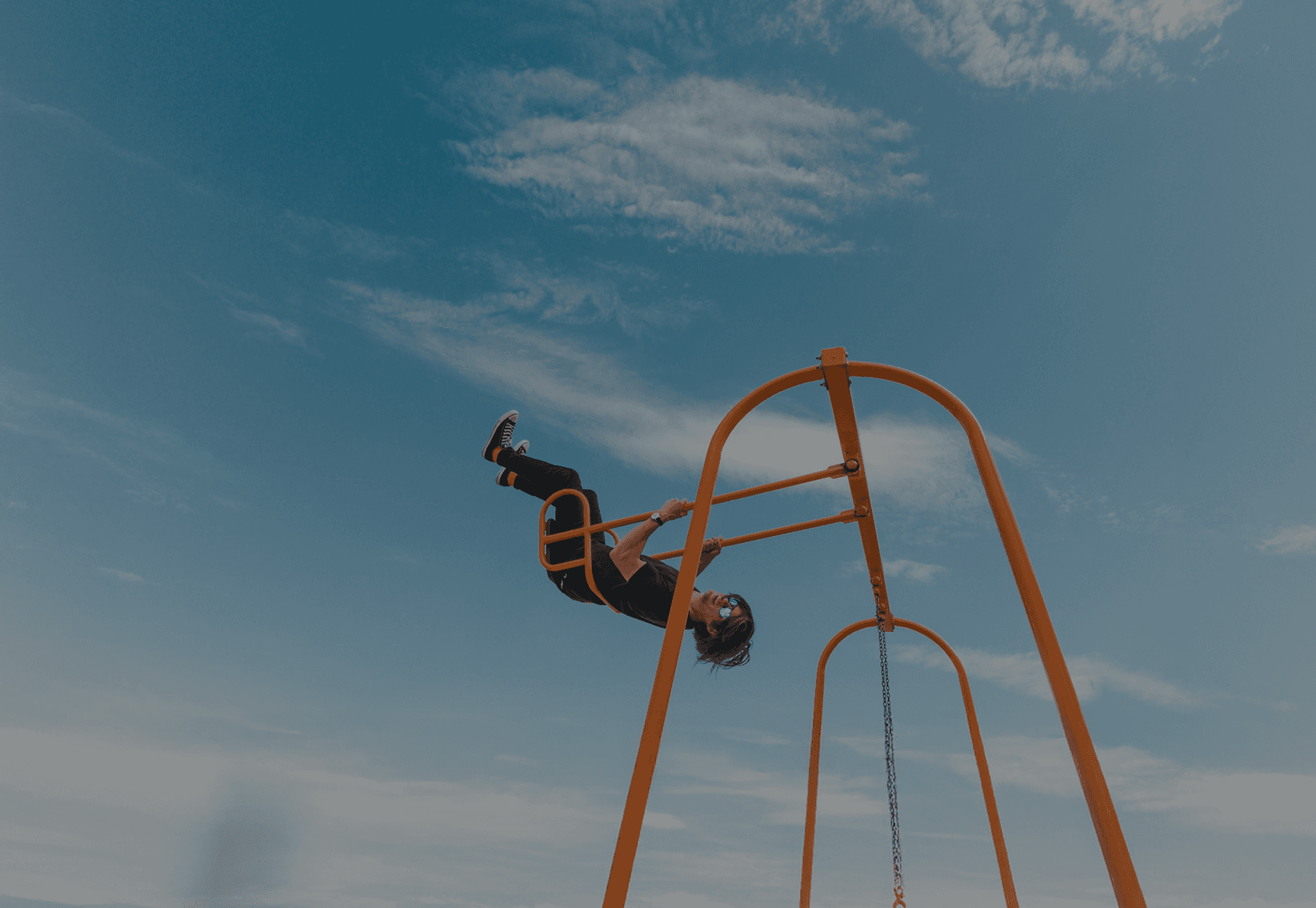 Person hanging upside down from orange playground bars against a bright blue sky.