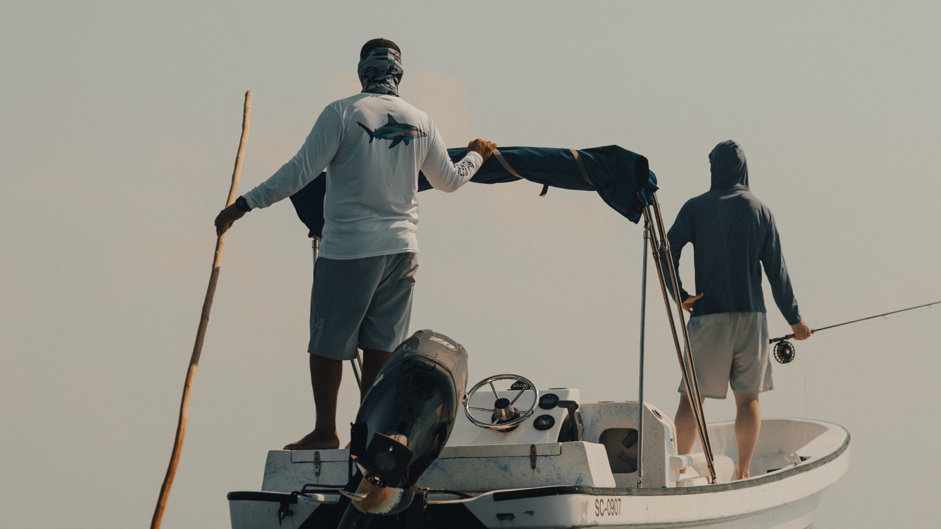 Fishing guide and angler on a skiff in Belize. Guide is poling the boat and scouting for fish.