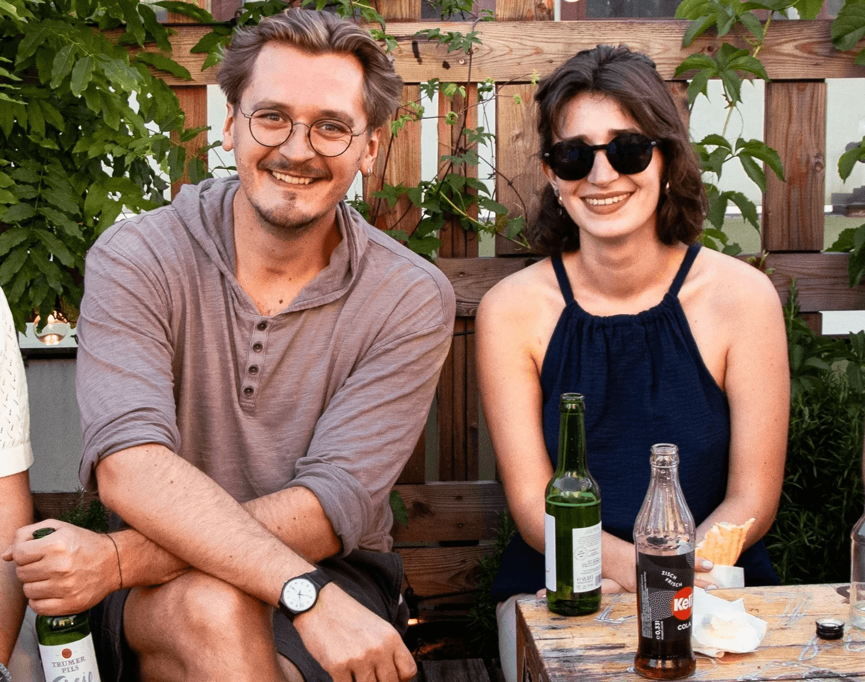 Ein junger Mann und eine junge Frau sitzen lächelnd nebeneinander und unterhalten sich an einem Stammtisch