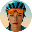 Close-up of a woman in a teal cycling helmet and orange sunglasses, looking at the camera.
