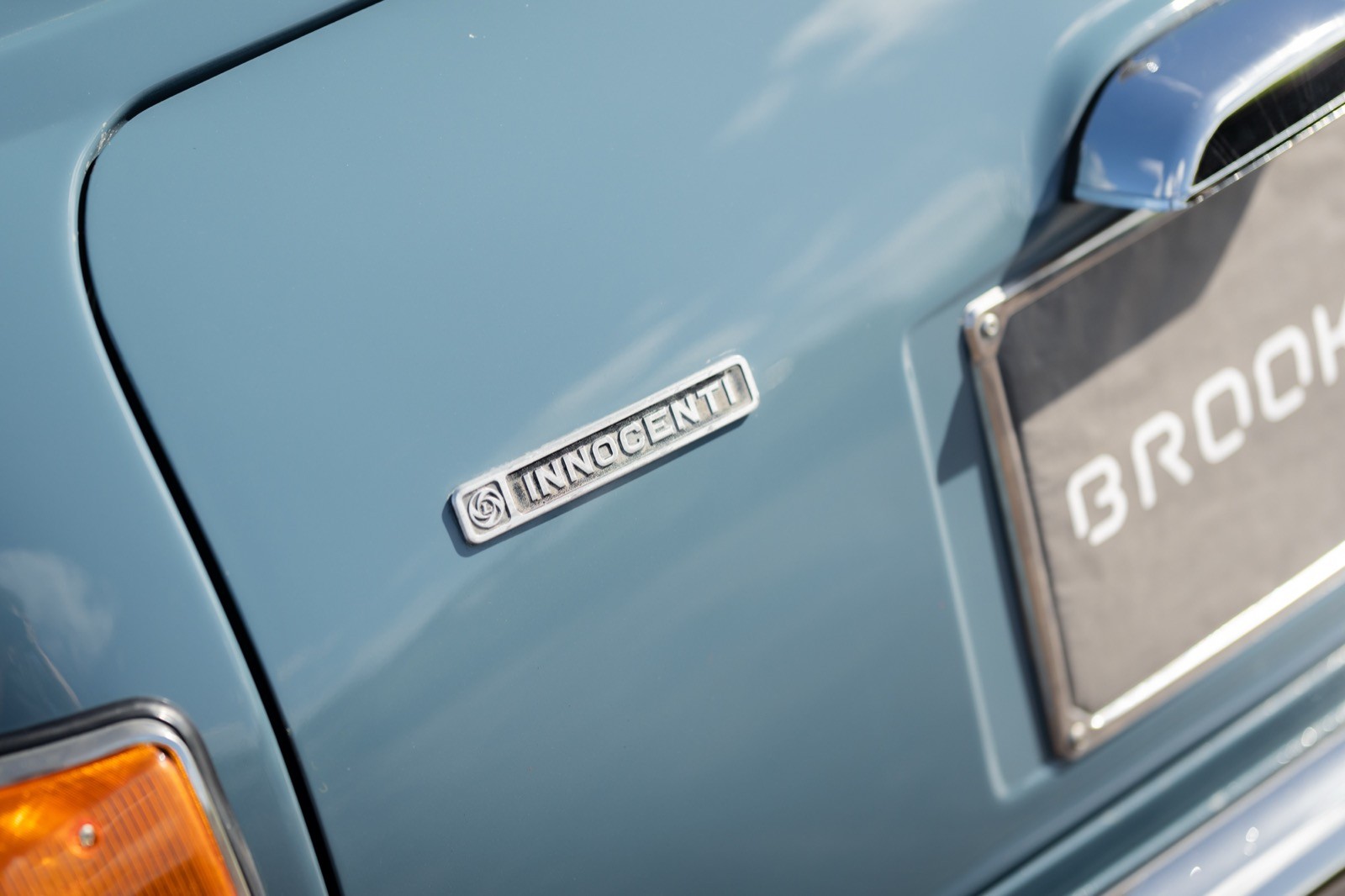 Close-up of a blue car's rear door, featuring a chrome emblem and part of the license plate area.