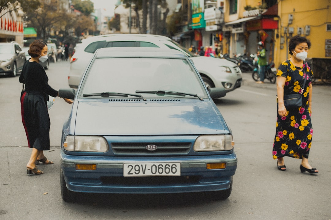 a woman in a black dress standing next to a blue car