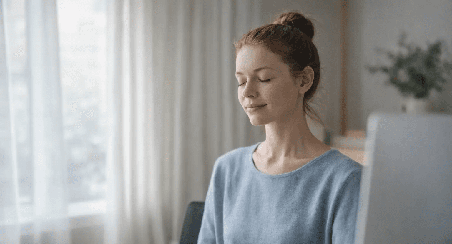 Femme assise à un bureau, les yeux fermés, pratiquant une respiration consciente dans un environnement de travail calme et lumineux