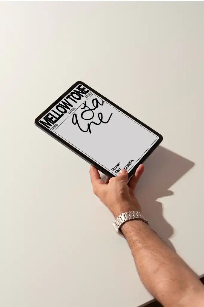 Close-up of a hand holding an iPad displaying the cover design, featuring  with handwritten text. The arm's shadow adds depth to the minimalist white background, creating a modern and clean aesthetic.