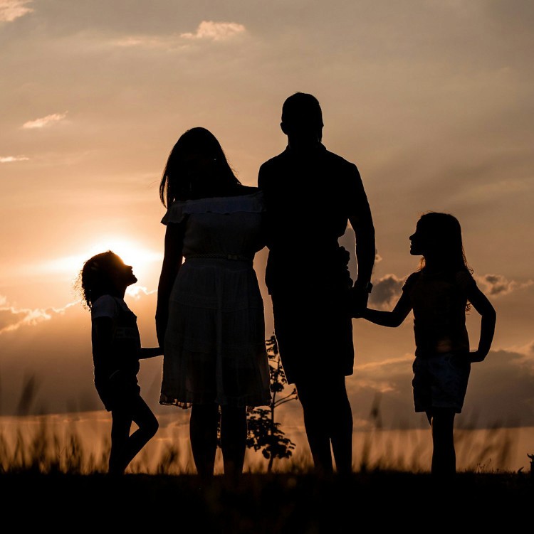 A family of two parents and two daughters facing the sunset at dusk, holding hands