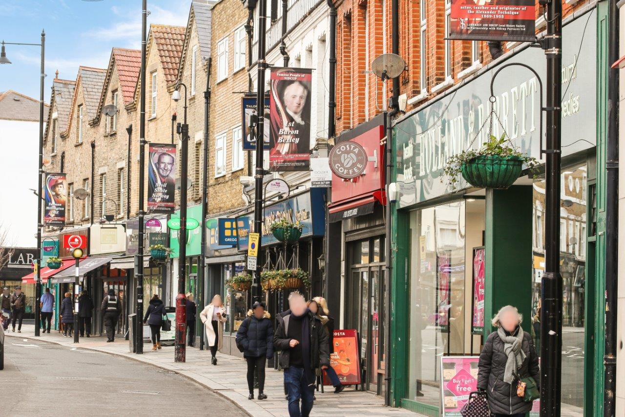 A smiling man with curly hair is sitting at a desk, looking at the camera, with a laptop and a lamp in the background.