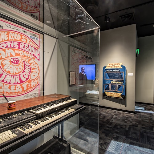 Muzejní expozice obsahující vintage klávesnici, velký plakát, obrazovku a starý rozhlasový přístroj ve stylu jukeboxu.