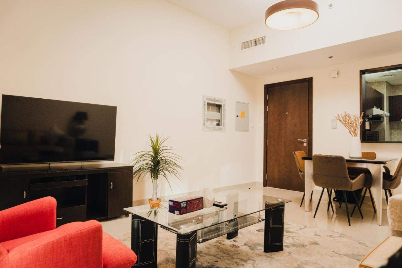 Al Ashrafia Holiday Homes at Dubai Sports City with a TV unit, glass coffee table, dining area, and bright interiors. 