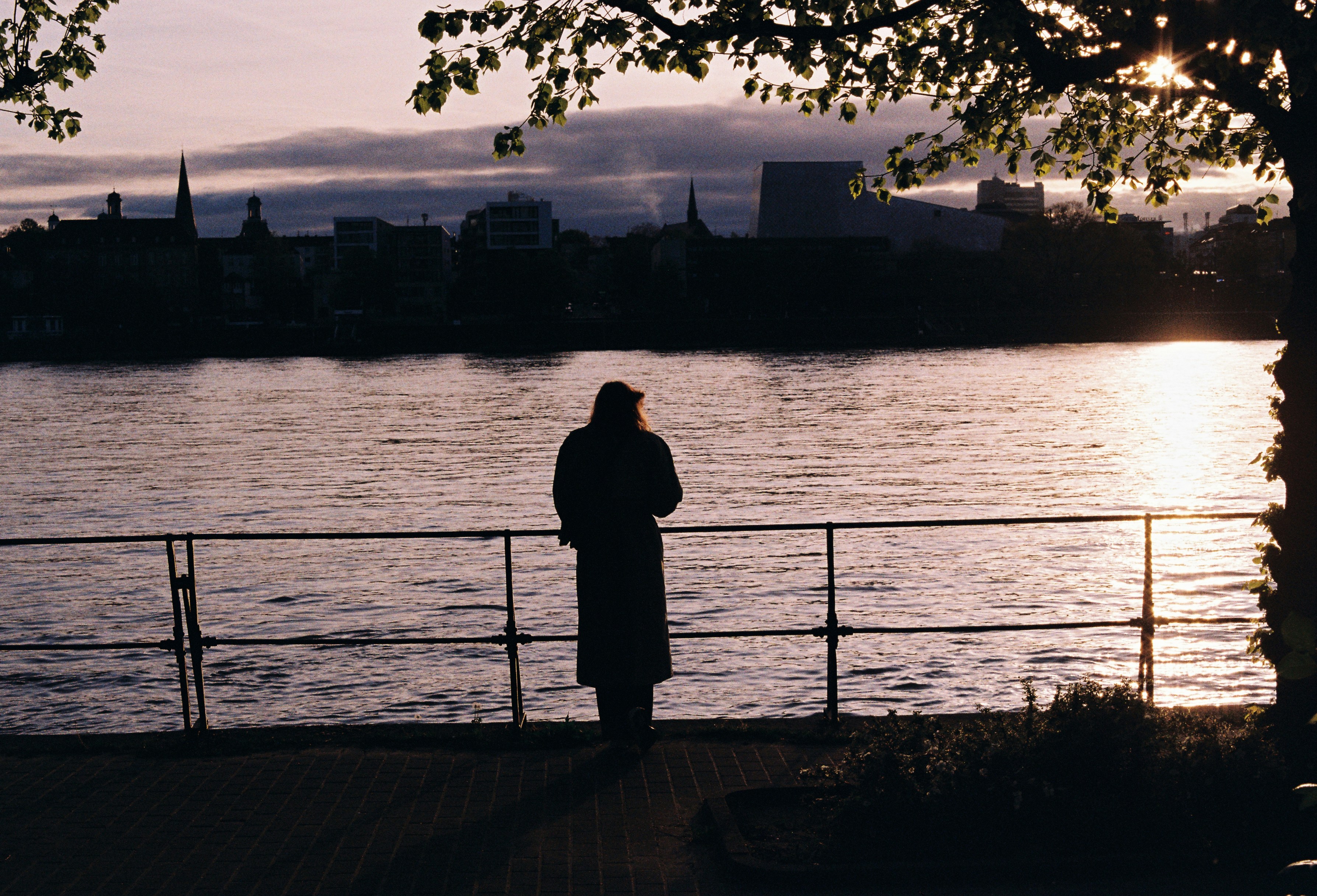 Person looking at sunset over water with city skyline.