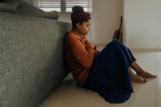 Photo of woman sitting on floor next to a couch with arms crossed