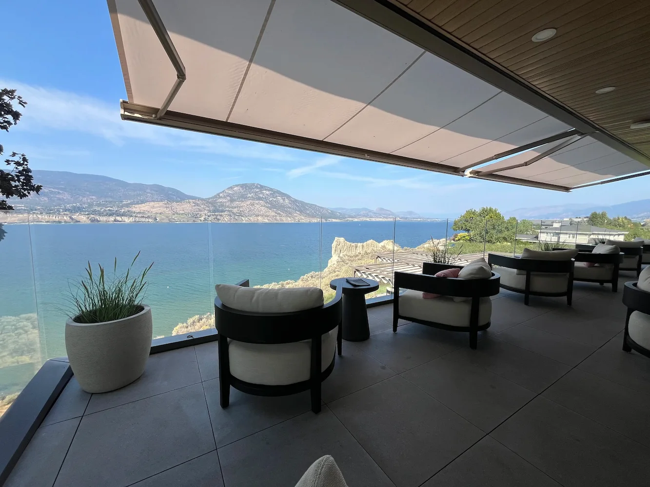 Luxury oceanview patio with frameless glass railing and lounge seating beneath retractable awnings, providing unobstructed coastal views in BC.