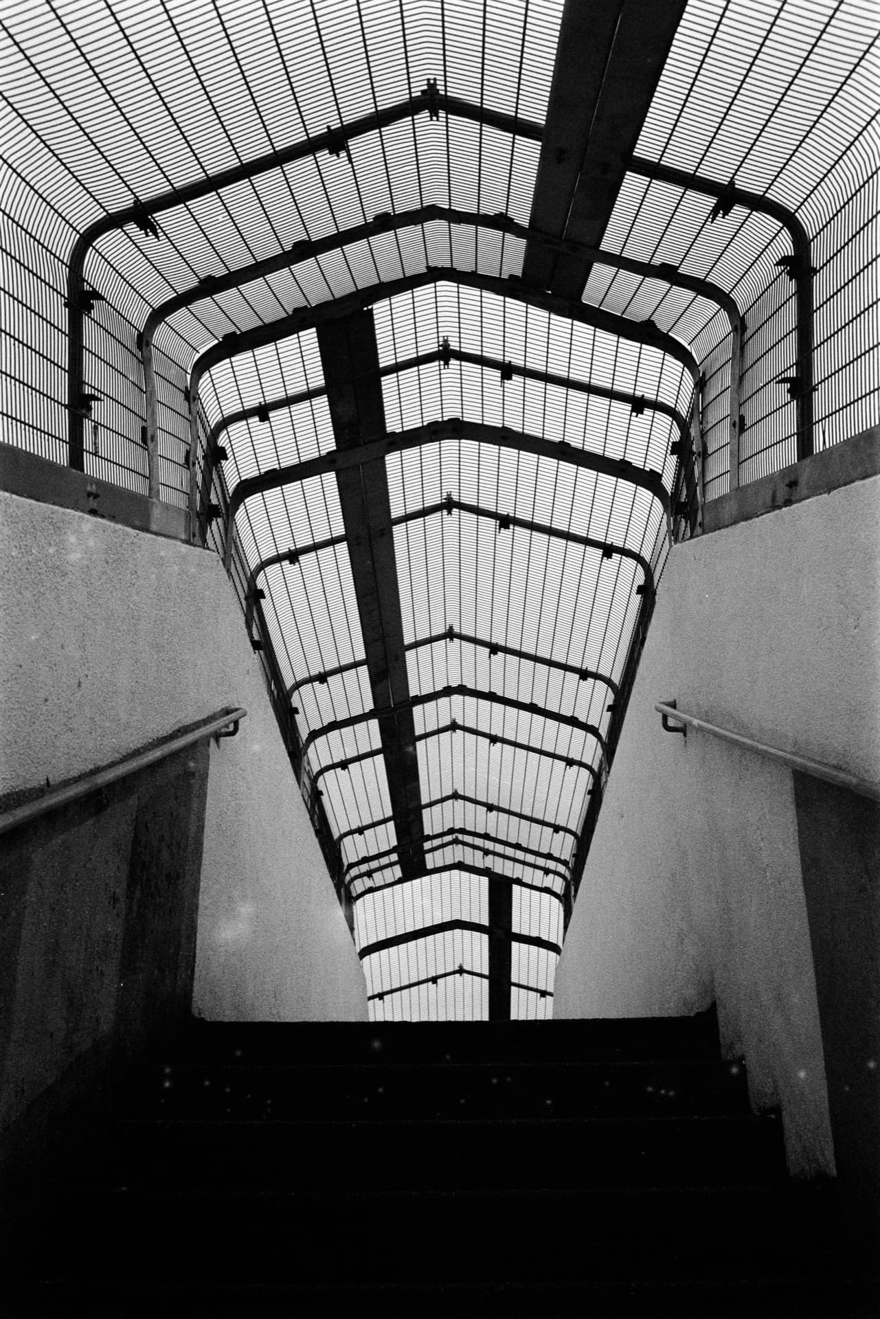 Curved steel footbridge canopy spanning railway tracks viewed from below