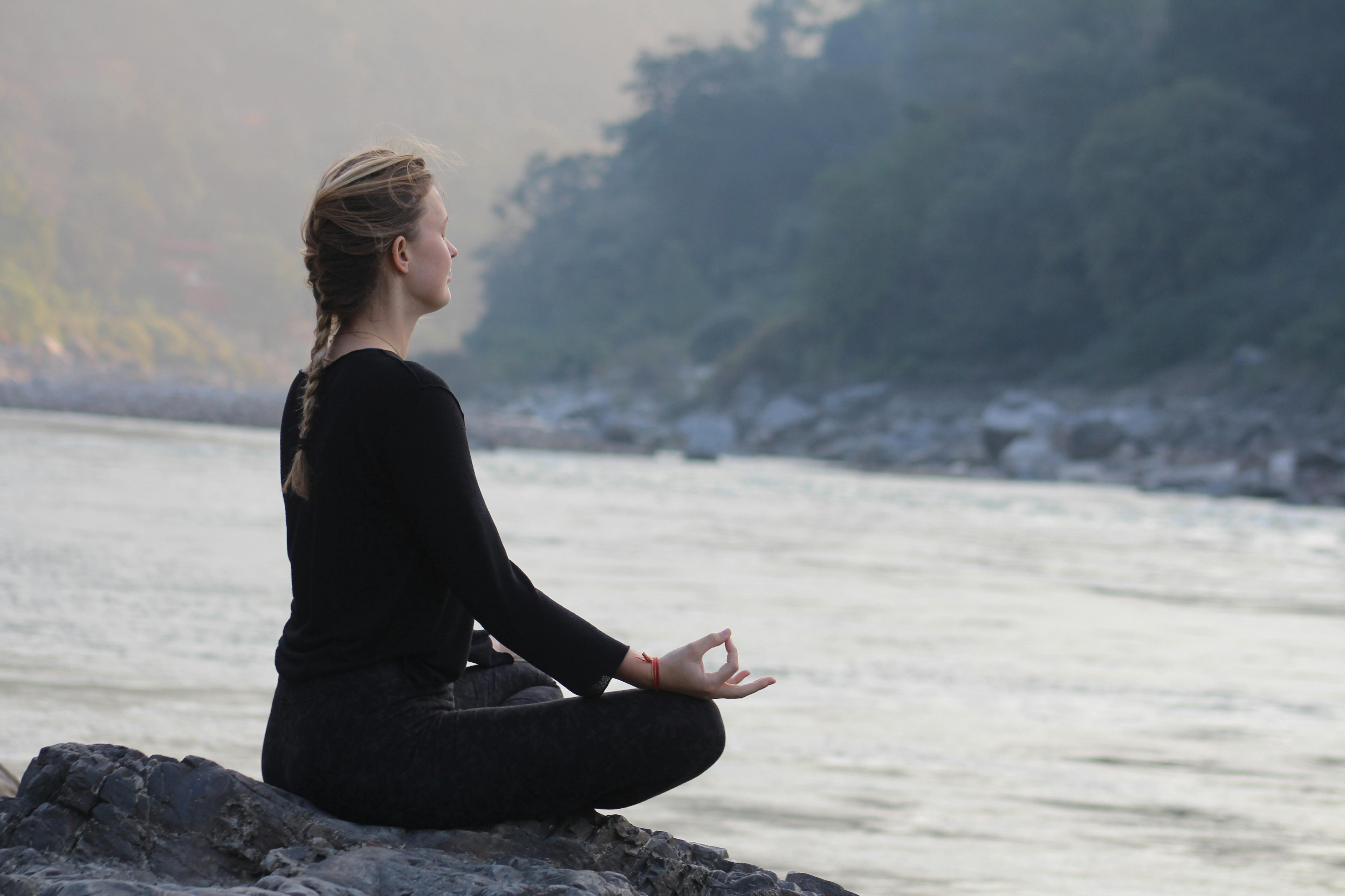 Woman meditating by a river, representing screen-free calm, self-reflection, mental health, and digital minimalism.