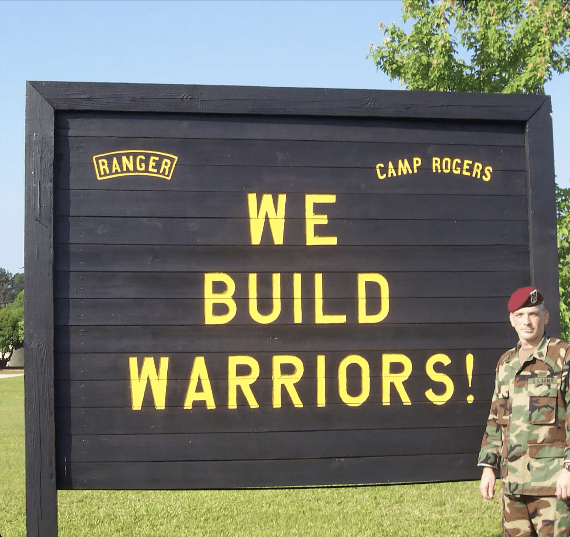 Robert Carrigg standing beside a “We Build Warriors” sign reflecting Carrigg’s veteran-led construction values