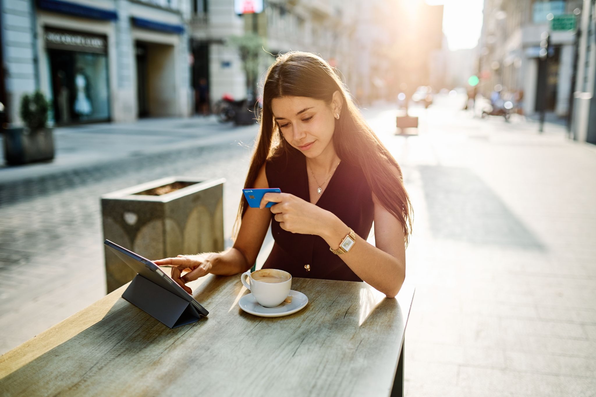 Woman using tablet and smartphone at outdoor cafe table with coffee.