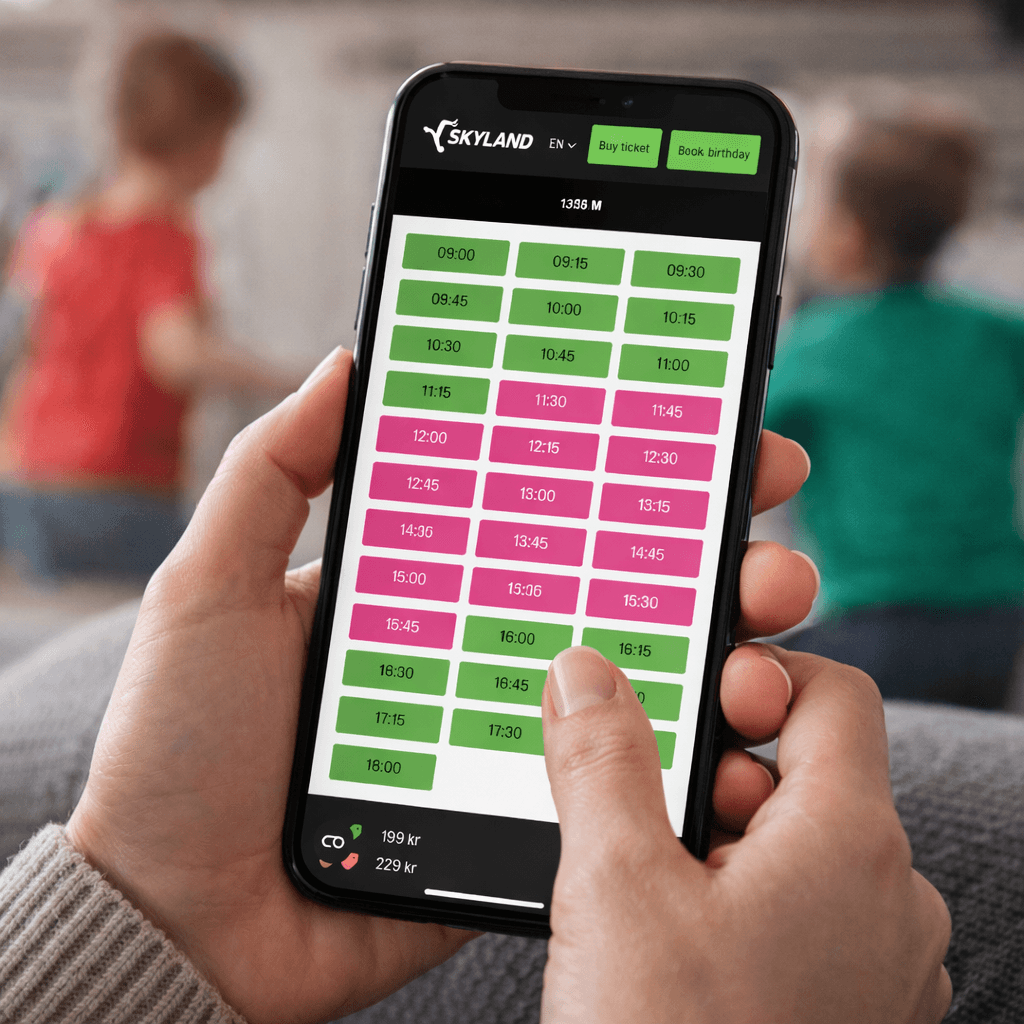 A young person with curly hair smiles at the camera while sitting in front of a laptop against a dark background.